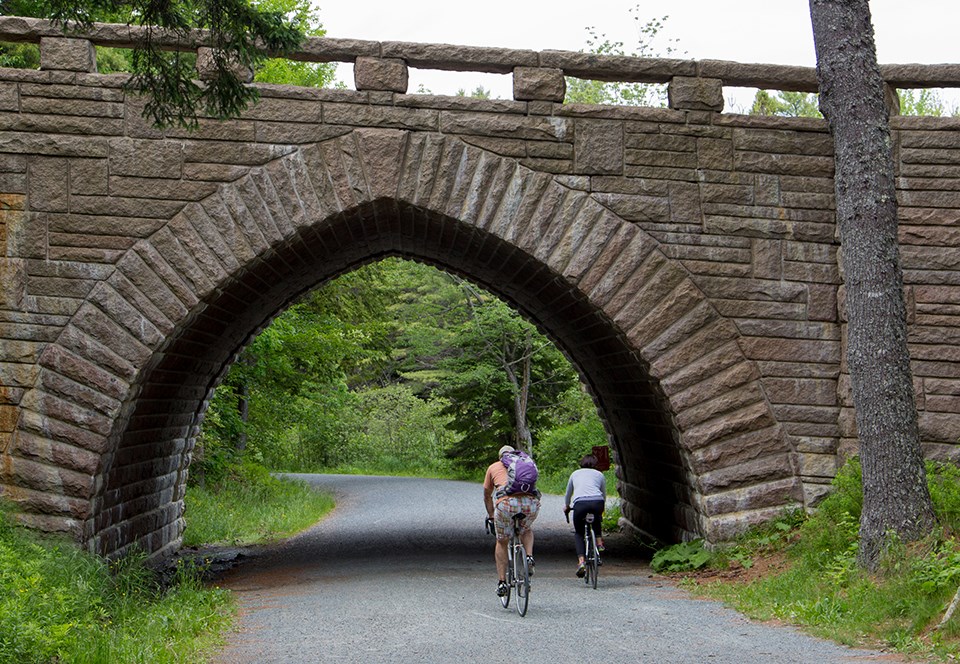 Two horseback riders under a stone bridge