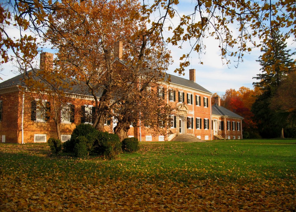 Black and white photo of large brick house with Civil War wagon and a number of trees in front