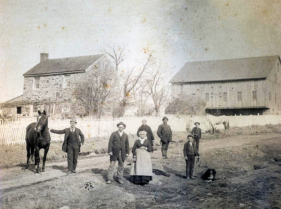 A black and white picture of a large african american family, a horse, a dog, and a house and barn.