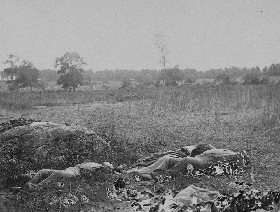 This view looks southwest, away from the Rose Woods. Three dead soldiers lie next to a large rock.