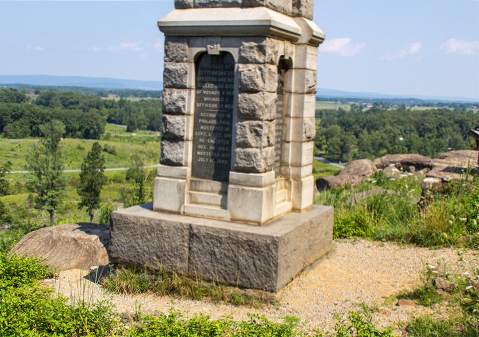 A crowd of people pose for a picture in front of the 91st Pennsylvania monument on the summit of Little Round Top.