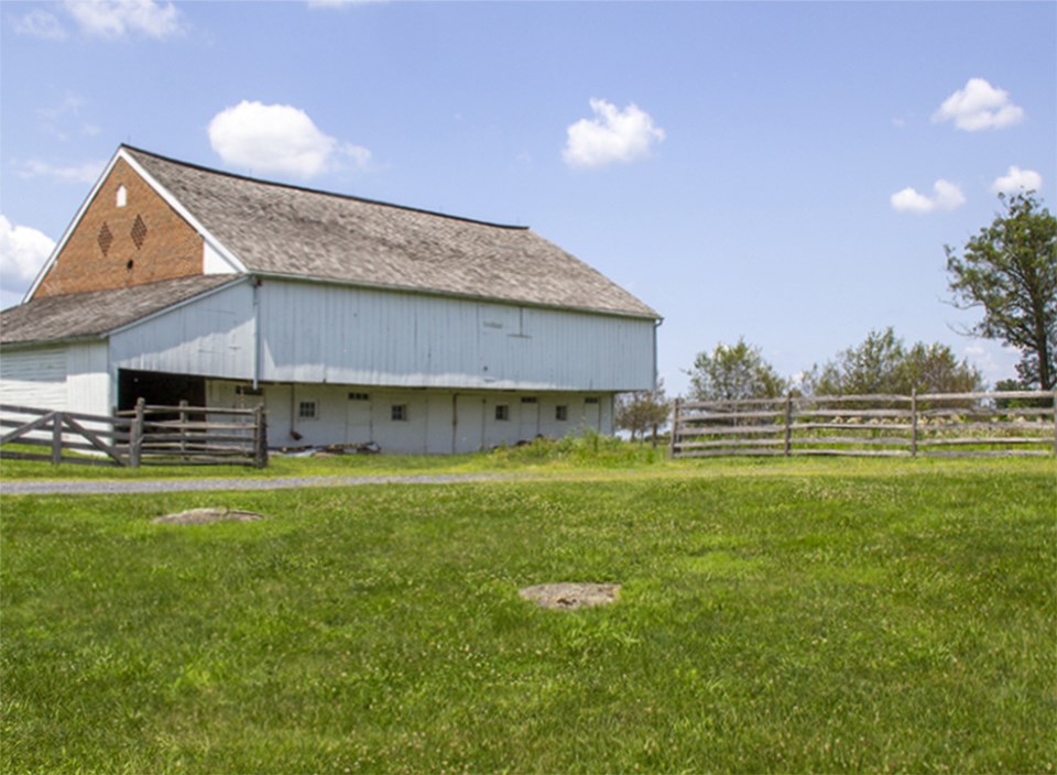 Dead horses scatter the ground in front of a large brick barn with single cannonball hole.