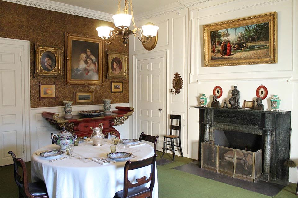 Black and white photograph of room with round table at center, paintings on walls