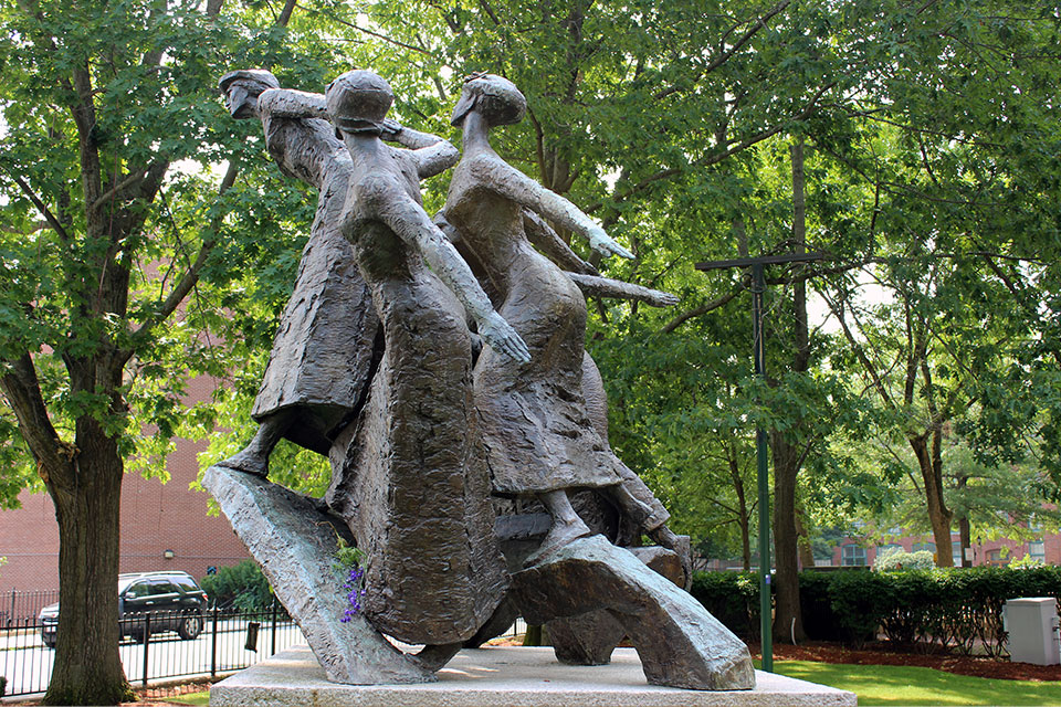 Plaster women figures usher forward on a pedestal.