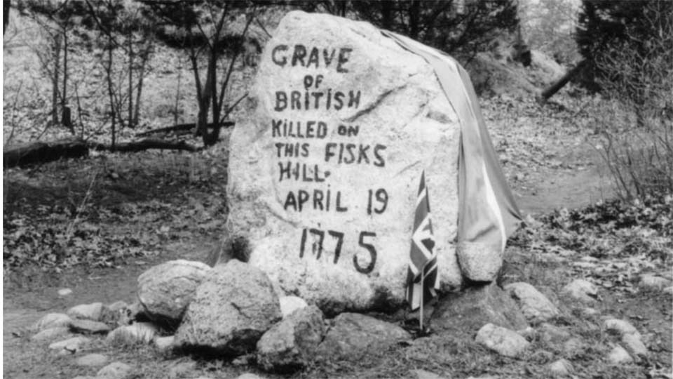 A black and white image of a large stone painted to mark the British Grave. Trees surround the stone.