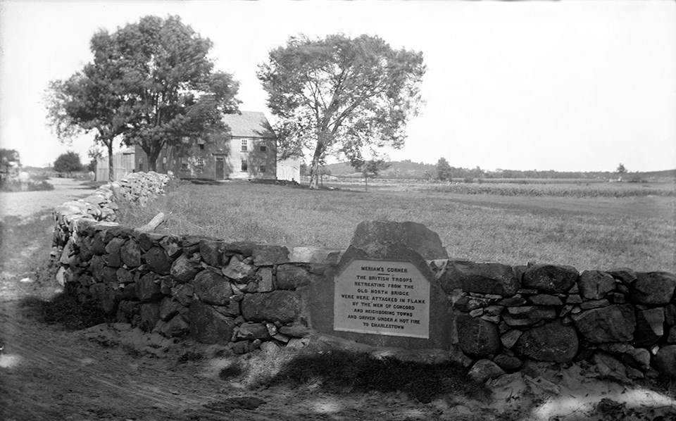 A stone monument set into a crumbling stone wall. Bushes and tress obscure an open field behind