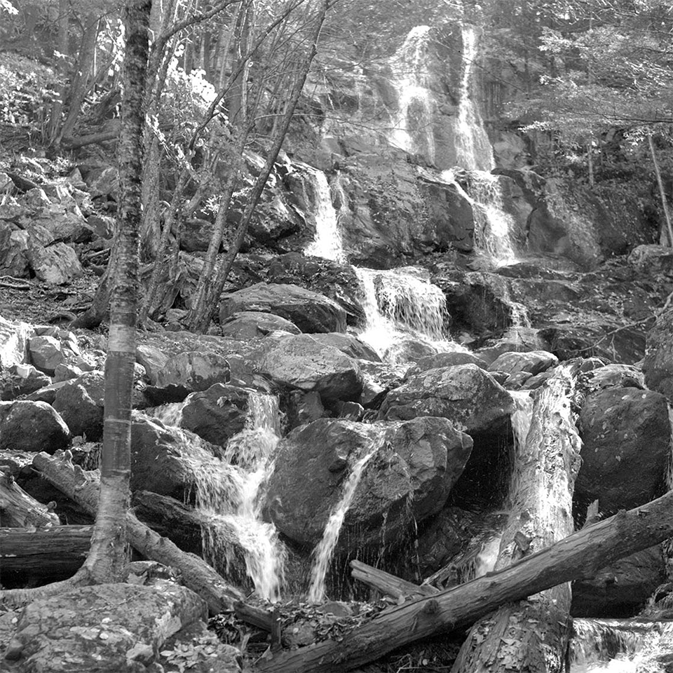 A black and white photograph of a tall waterfall in a forest.
