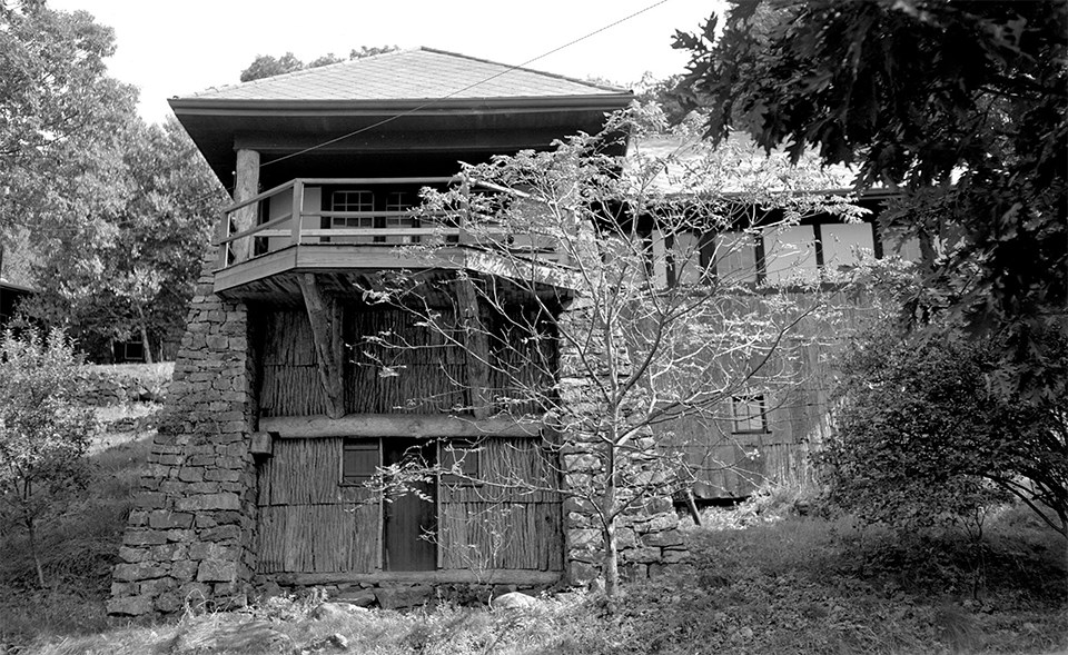 A black and white photograph of a rustic two-story cabin.