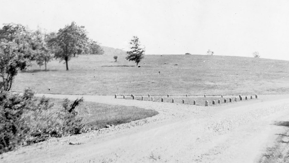 A black and white photograph of a road with a fork in it and bare ground all around.