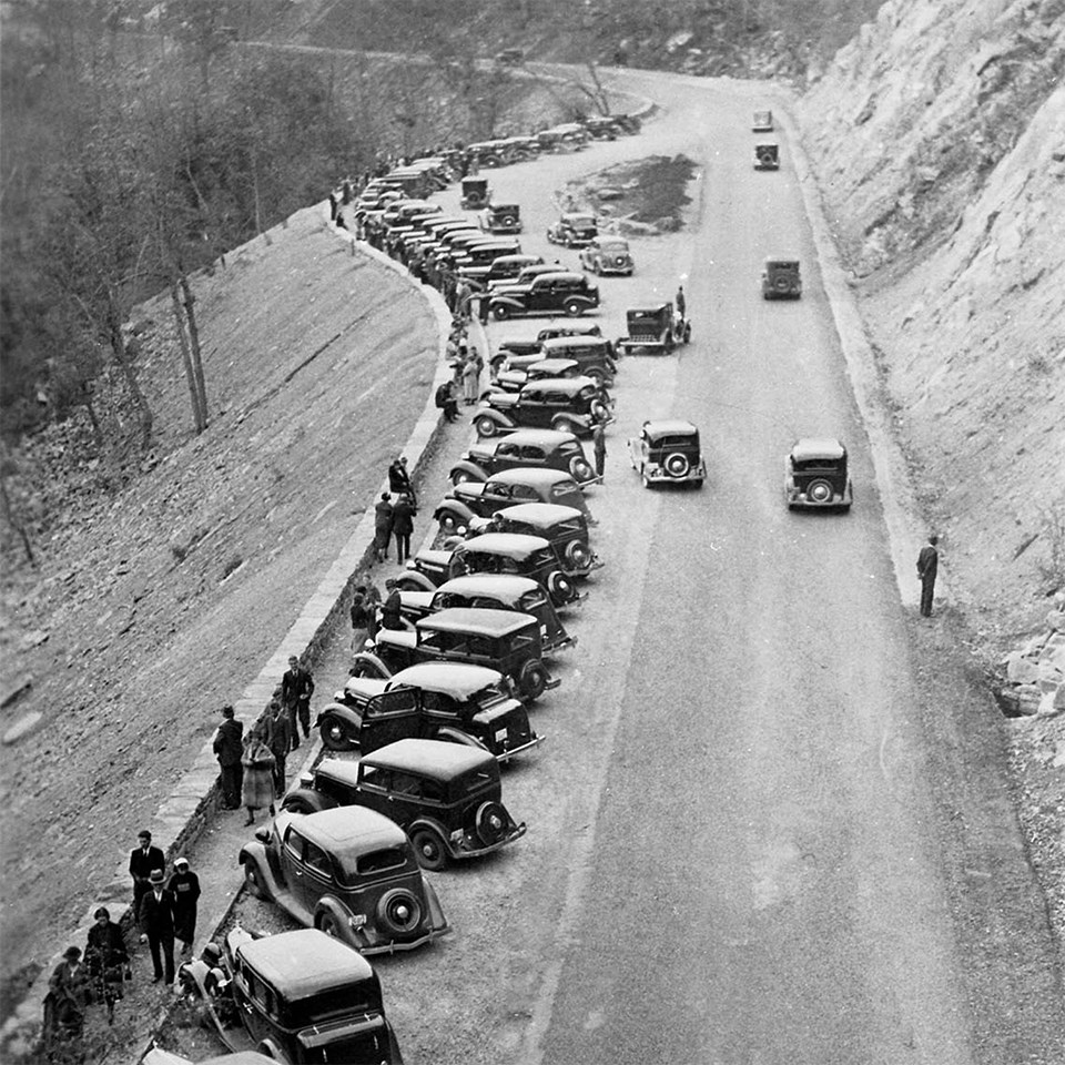 A black and white photograph from above looking down at a long overlook with lots of vehicles.