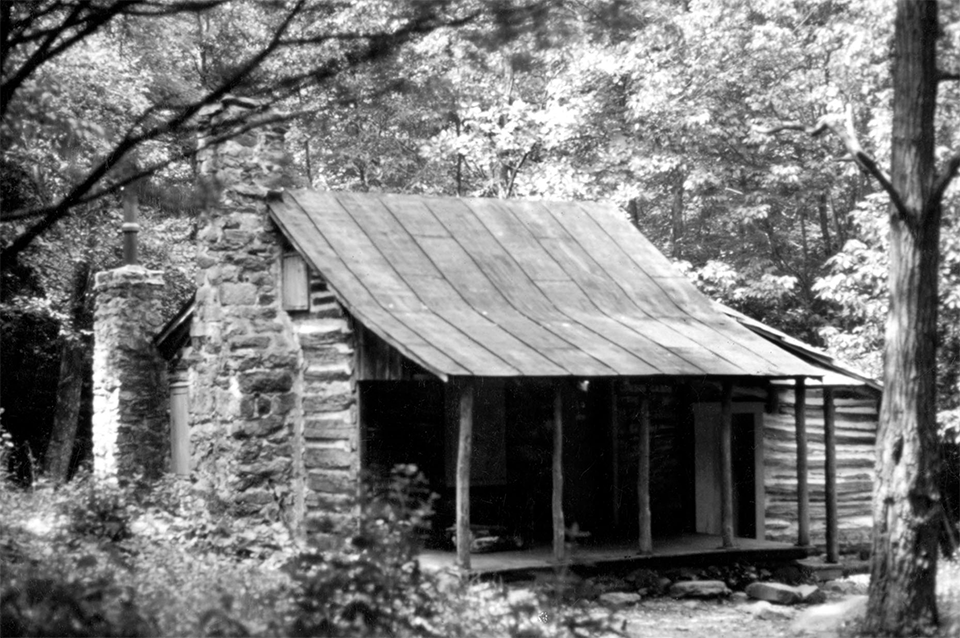 A black and white photograph of a log cabin in the woods.