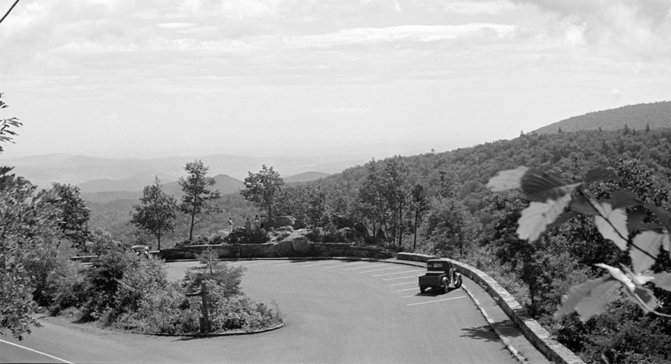 A black and white photograph of an overlook with mountain sin the distance.