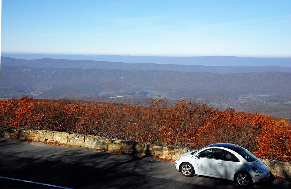 A black and white photograph of an overlook with a vehicle and valley in the distance.