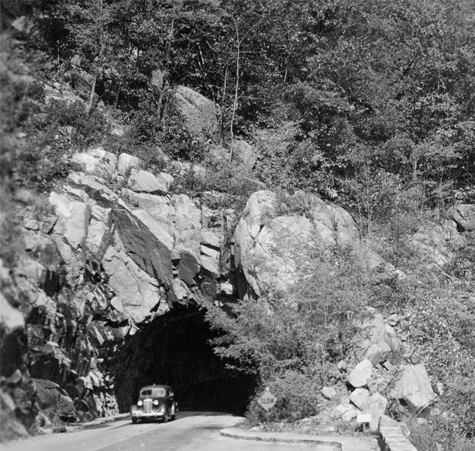 A black and white photograph of a car coming through a tunnel.