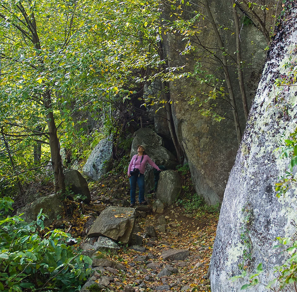 A black and white photograph of a person standing on a trail along a mountainside.