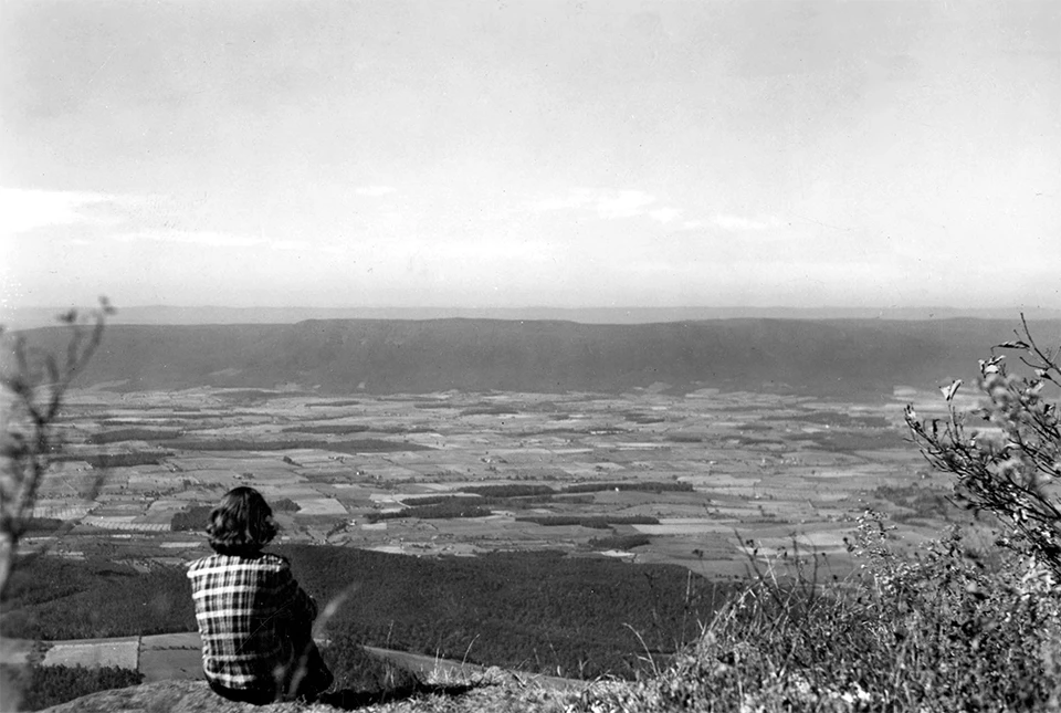 A black and white photograph of a girl looking over a distant valley.