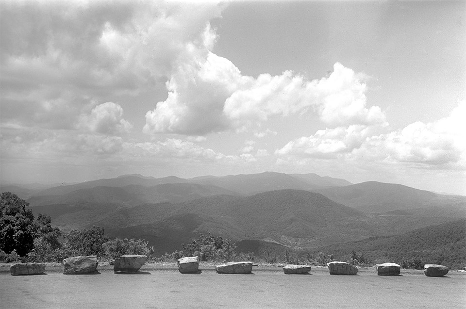 A black and white photograph of an overlook with mountains in the distance.