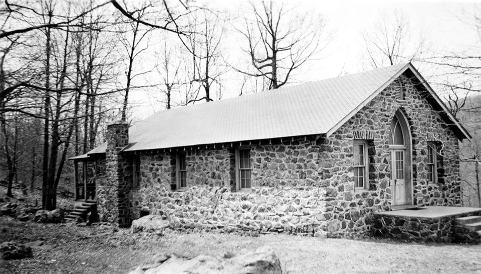 A black and white photograph of a stone building in the woods.