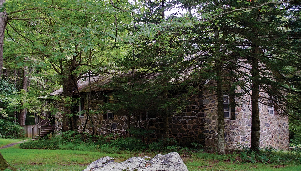 A black and white photograph of a stone building in the woods.