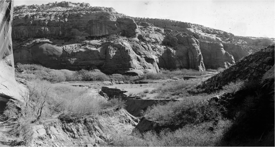 Black-and-white photo showing sandy canyon bottom with sharp gully
