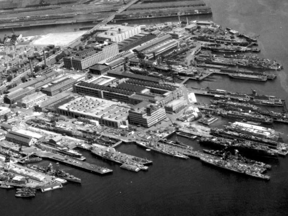 Photograph of roadways, piers, buildings, dry docks, and ships at a naval shipyard.