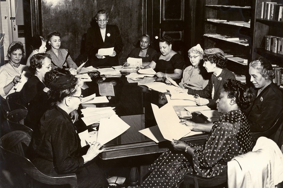 Historical black and white photo of a group of women sitting around a table