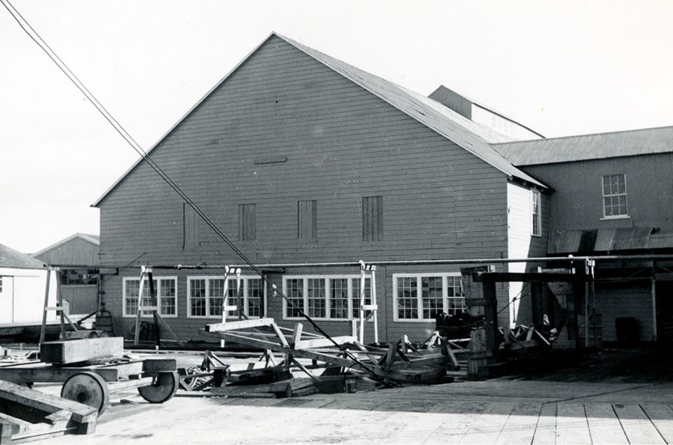 Equipment rests on the dock in front of a warehouse building with a peaked roof and low row of windows.