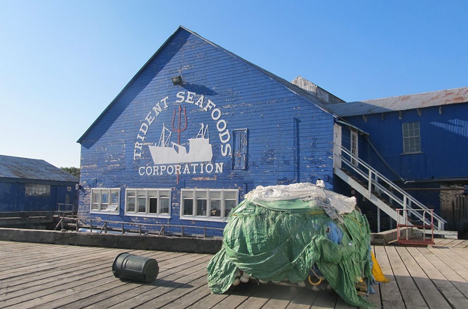 Equipment rests on the dock in front of a warehouse building with a peaked roof and low row of windows.
