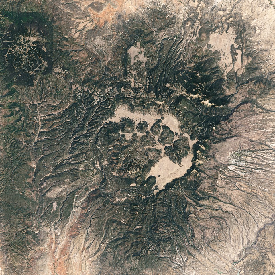 A satellite view of a caldera.  The depression resembles a crater with green hills inside.  Along the flanks, drainages fan out downhill.