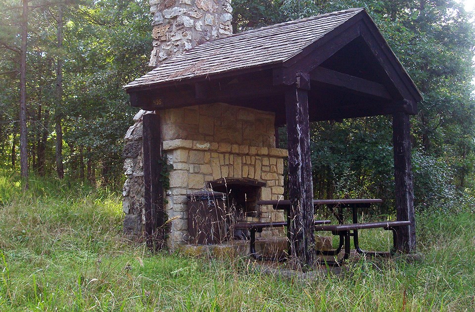 Historic image of four young women in dresses setting up a picnic at a table near a covered shelter.