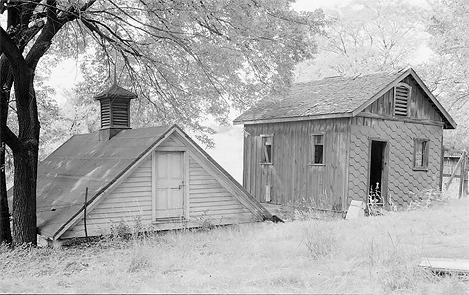 Historic black and white photo of a 19th century chicken house and ice house, side by side.