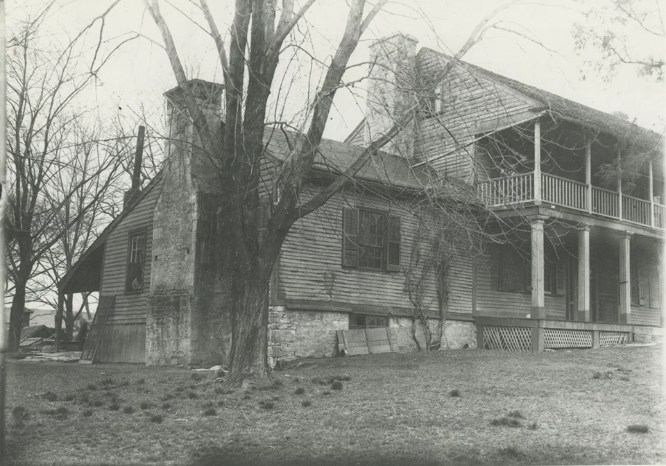 Black and white historic photo of a frame house with large stone chimneys