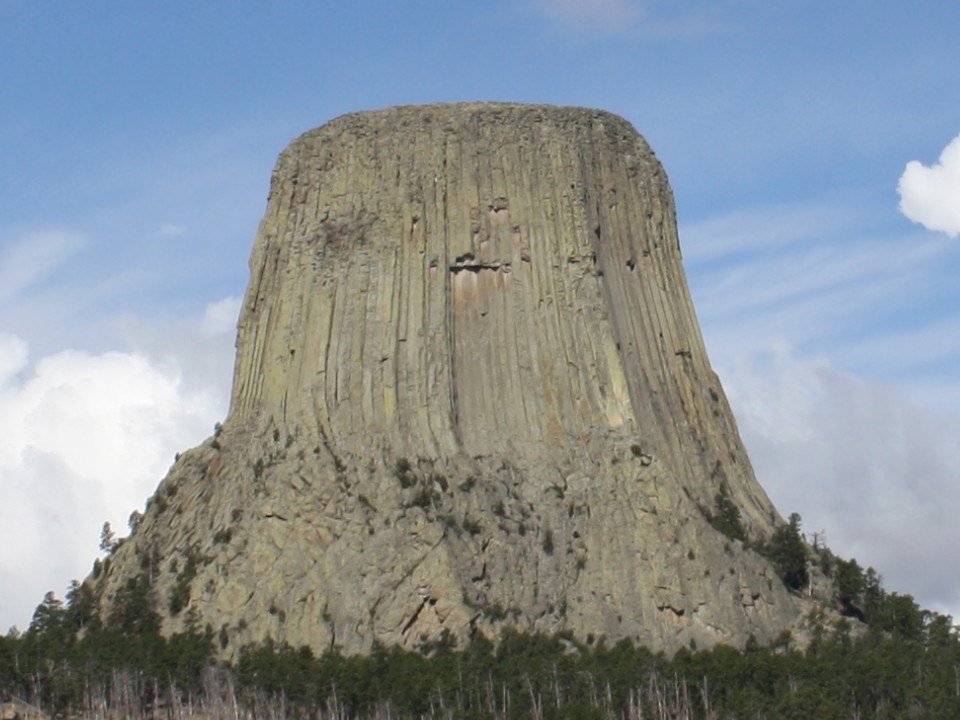 East face of Devils Tower with pine trees in foreground and blue sky background