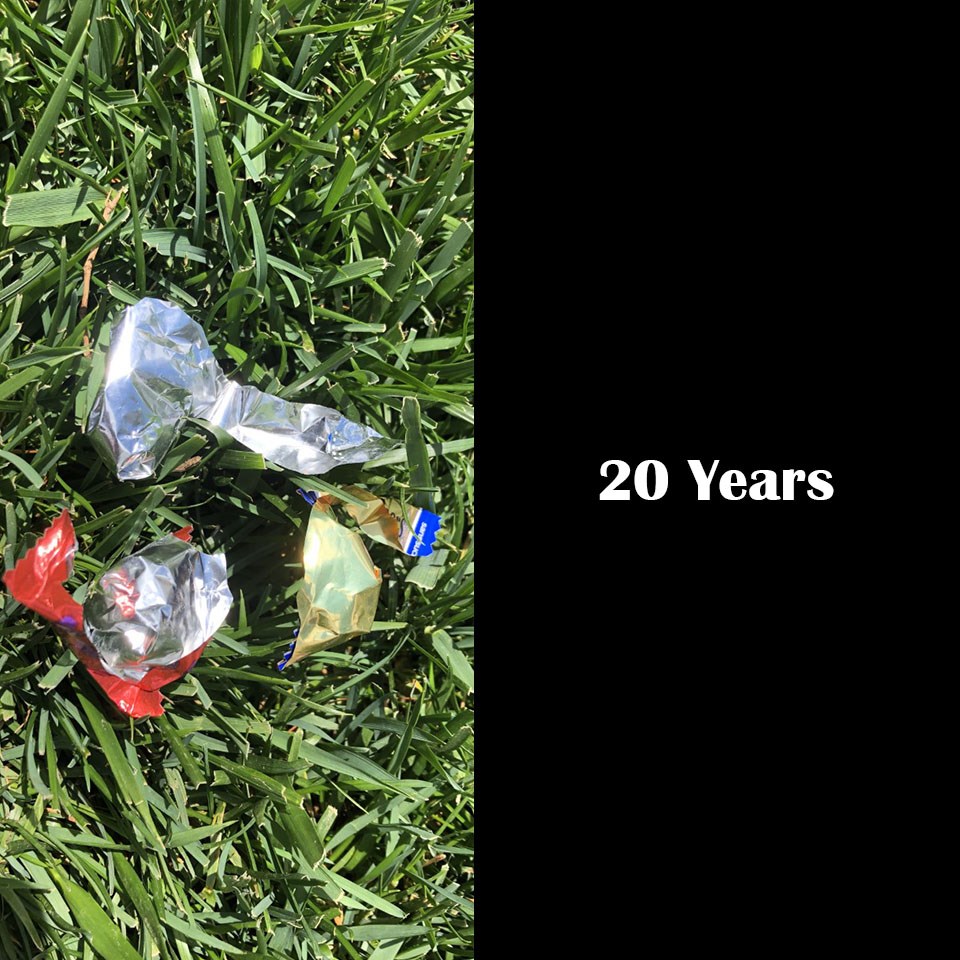 Silver, shiny candy wrappers on green grass, 20 years