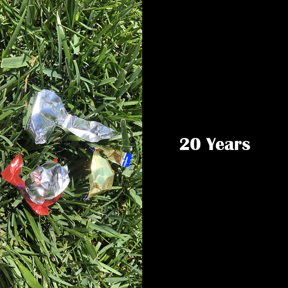 Silver, shiny candy wrappers on green grass, 20 years