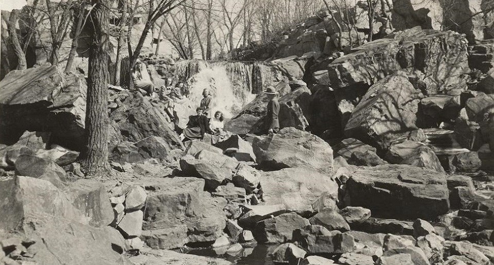 Black and white photo of people on rocks in front of a waterfall