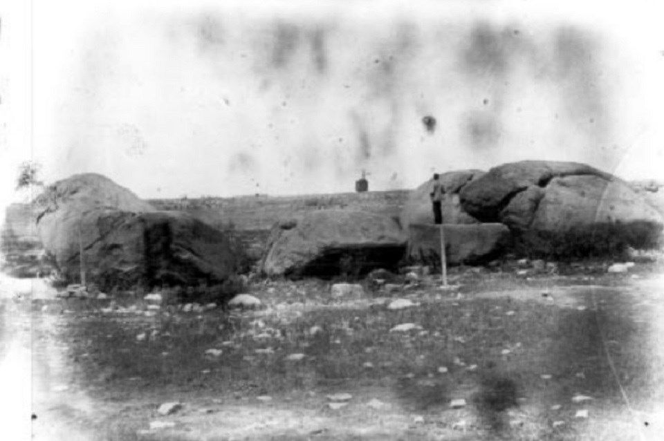 Old photo of man standing on boulders
