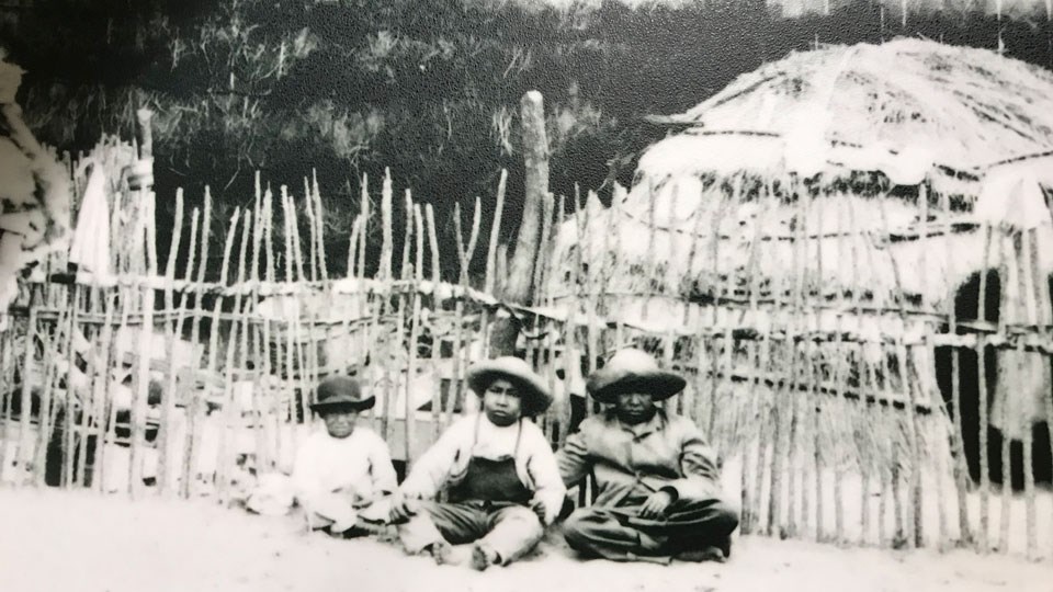 black and white photo of young boys in front of round thatched house