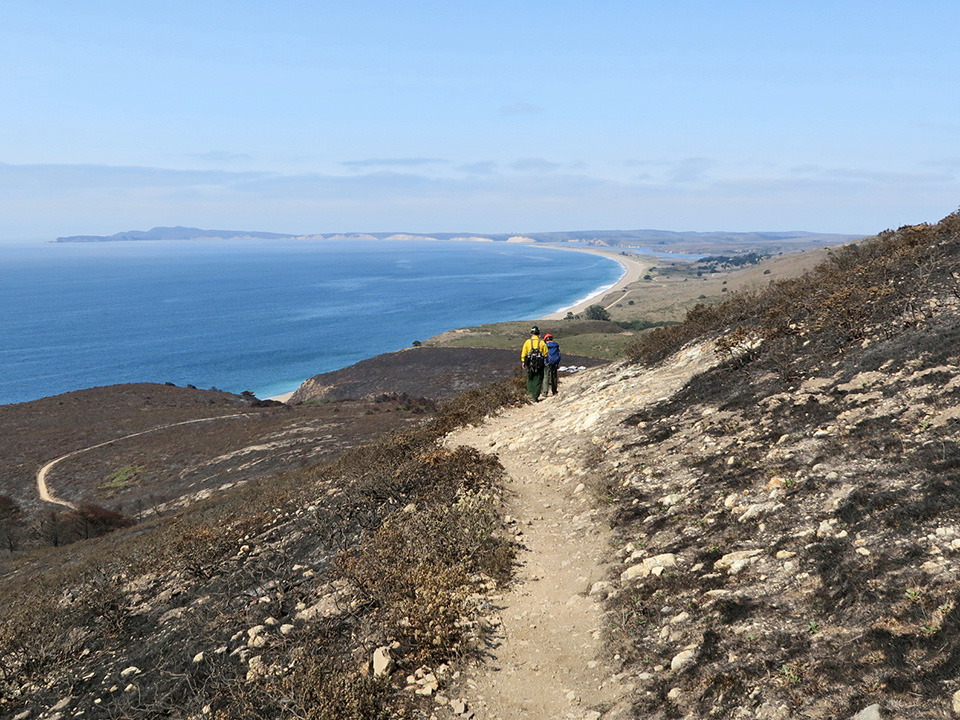 Expansive section of burned, blackened landscape, with beaches and bluffs beyond.