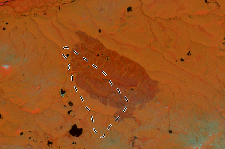 A Landsat image in orange hues of a fire scar with a dashed line denoting the original perimeter