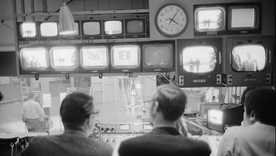 Black and white photo of three people sitting in front of many screens at WETA