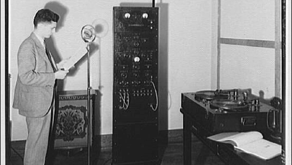 Black and white photo of a man standing at a radio recording setup in the 1920s