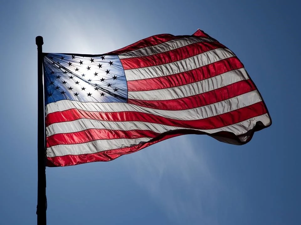 American flag waving in the breeze, the sun shining through the stars