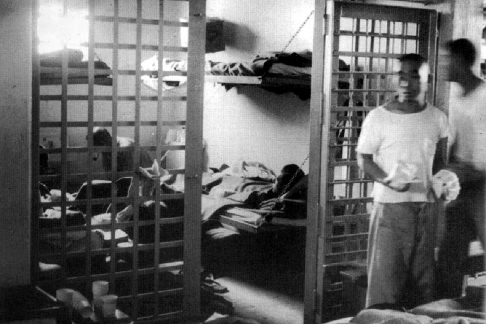 Historic black and white photo of several people in a jail cell with their personal belongings