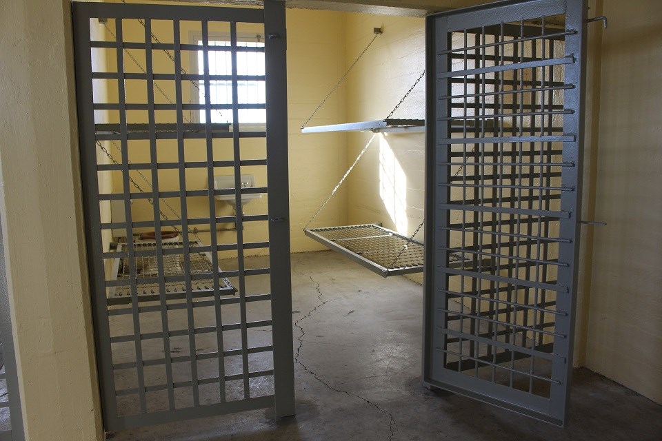 Historic black and white photo of several people in a jail cell with their personal belongings