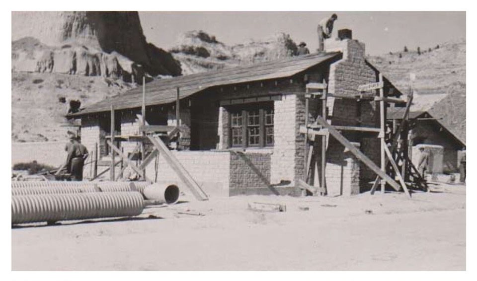 The scaffolding, drainpipes, and workers show the construction that is occurring on an adobe brick structure.