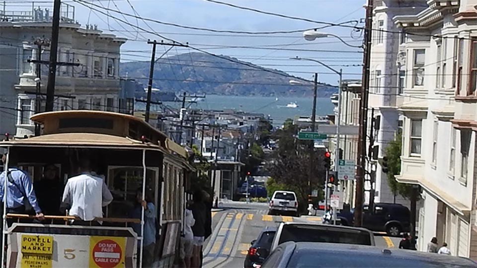 filled street car goes down busy street with view of Alcatraz