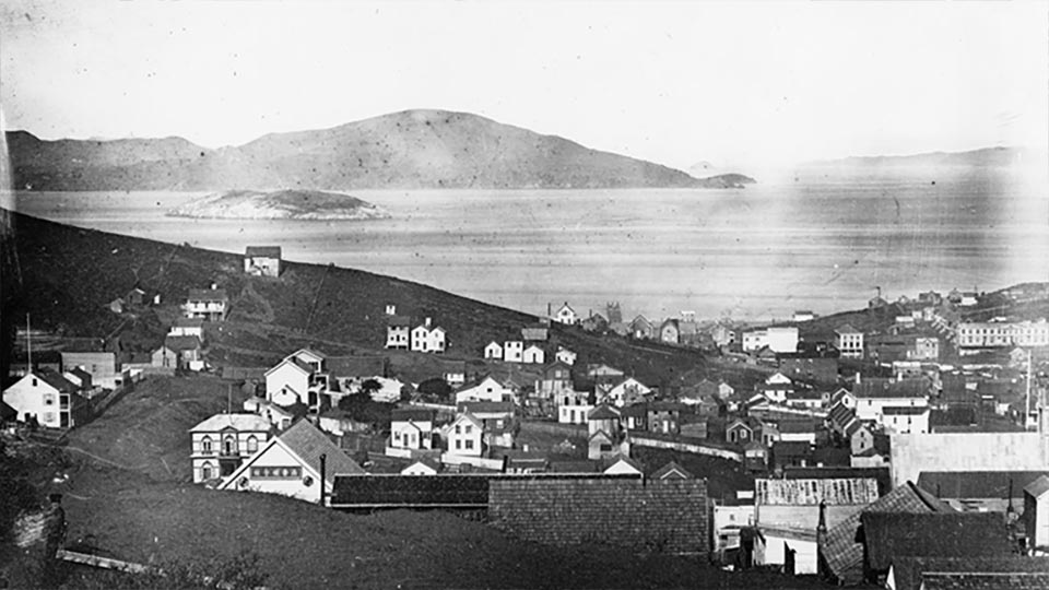 filled street car goes down busy street with view of Alcatraz