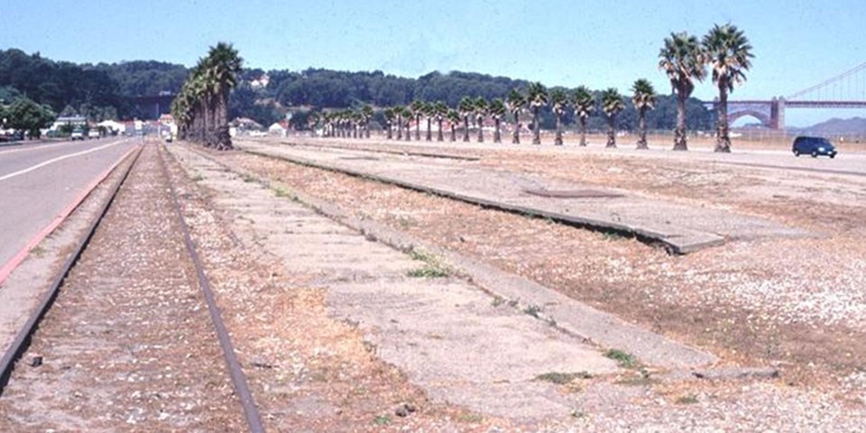 Image of crissy field before restoration: train tracks and empty land with little to no vegetation.