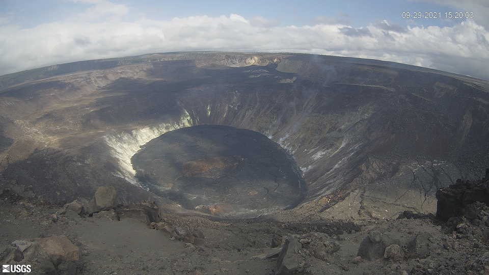 View looking down into deep large crater with dark brown surface and large flat bottom.